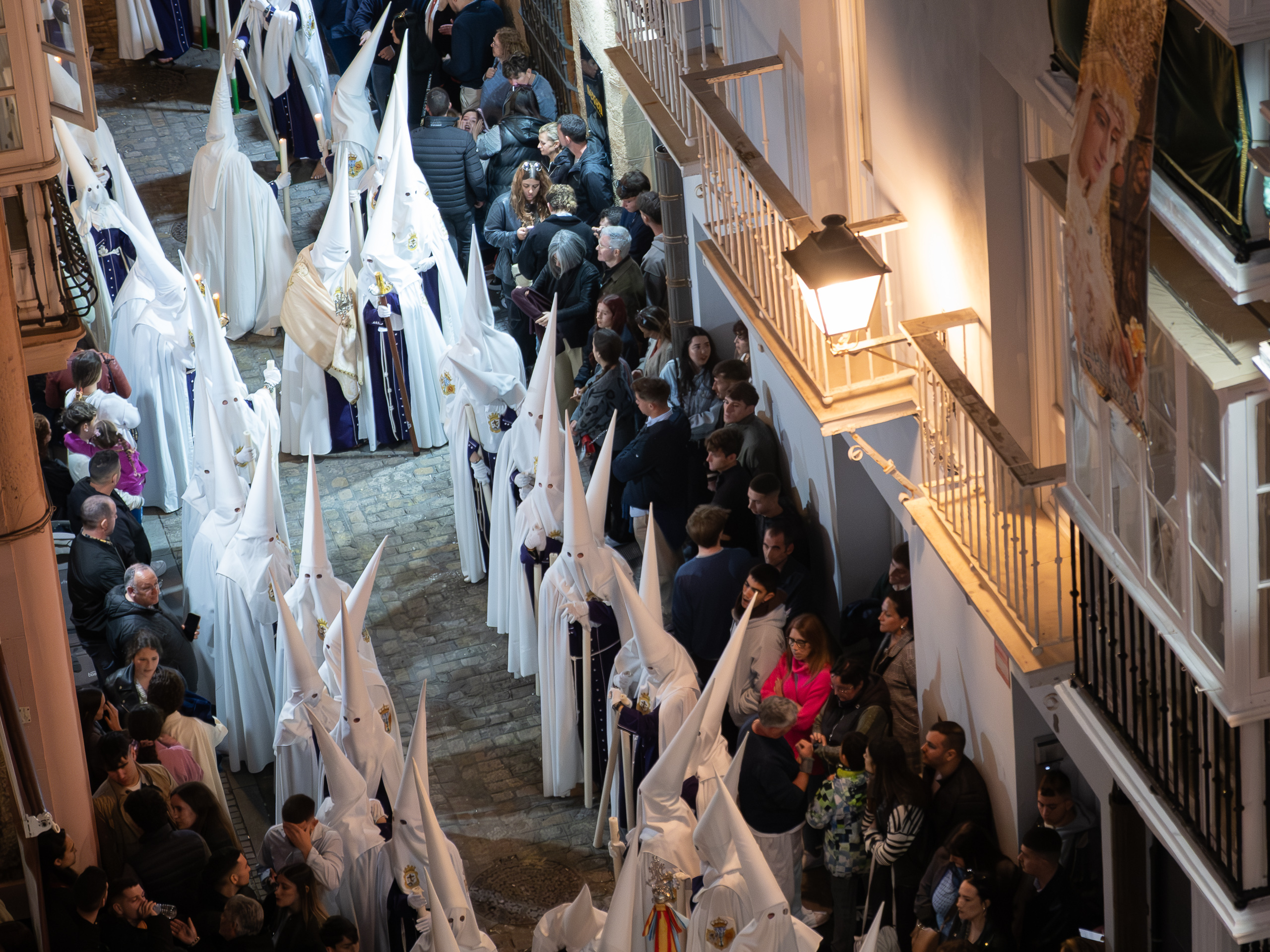 Weiße Nazarenos ziehen durch eine enge Gasse